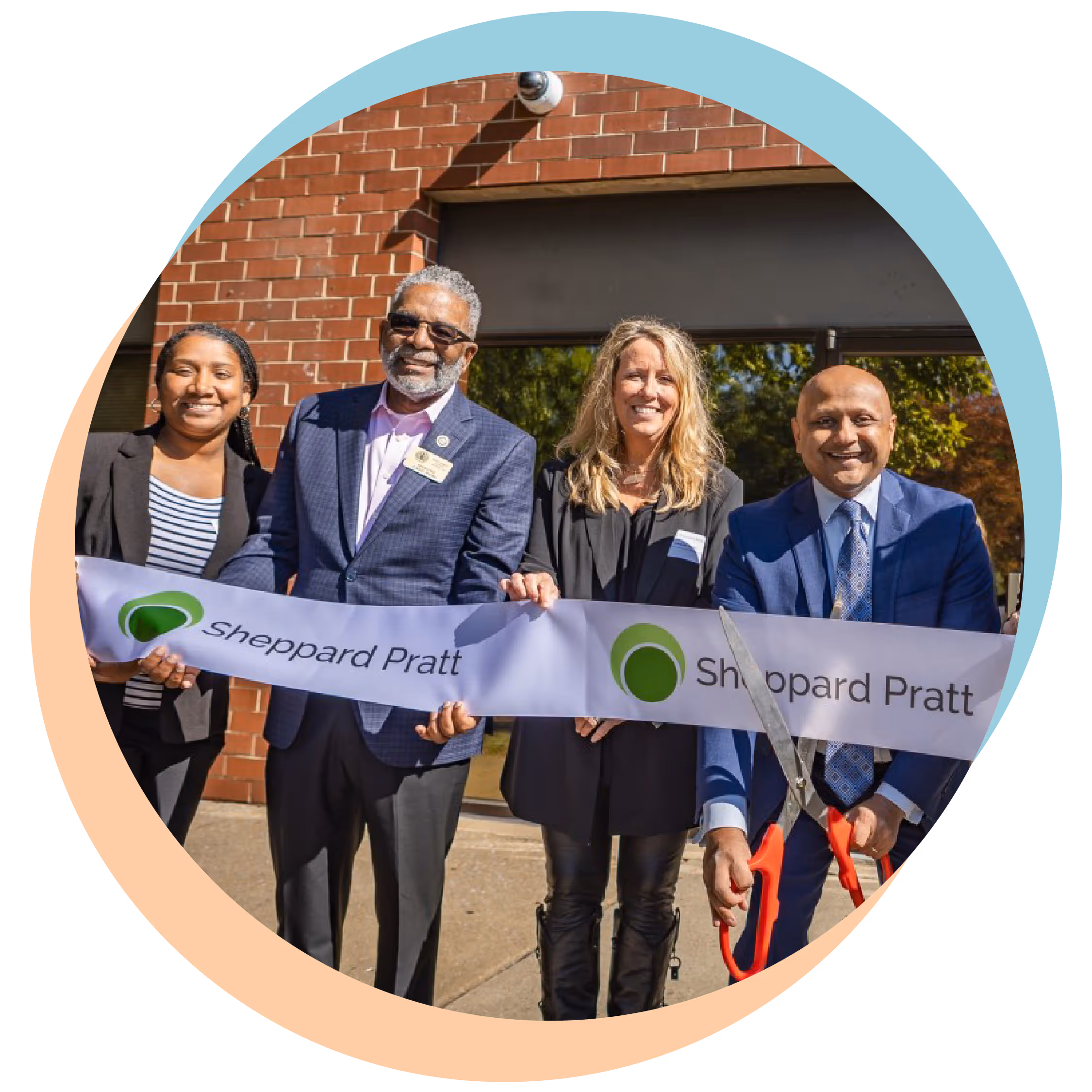 Four people smiling and holding a Sheppard Pratt ribbon for a ceremonial ribbon cutting event.