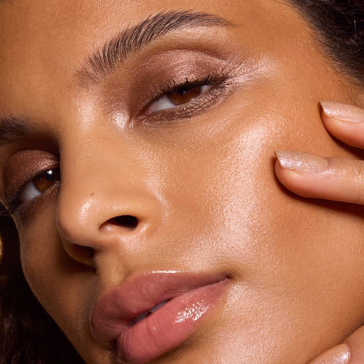Close-up beauty portrait with luminous skin and a hand touching the cheek