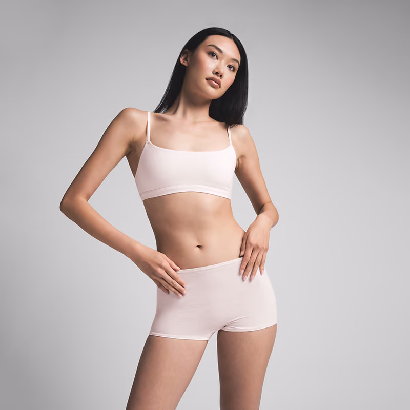 Model wearing a pale pink bra and shorts against a gray background