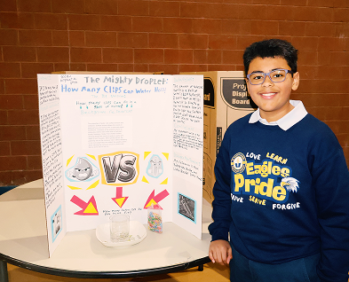 Student standing beside science fair project board about water droplets