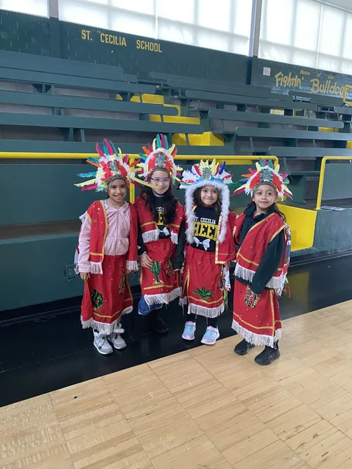 Four students in traditional cultural dance costumes in school gymnasium