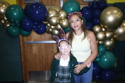 Student and adult posing at school celebration with balloon backdrop