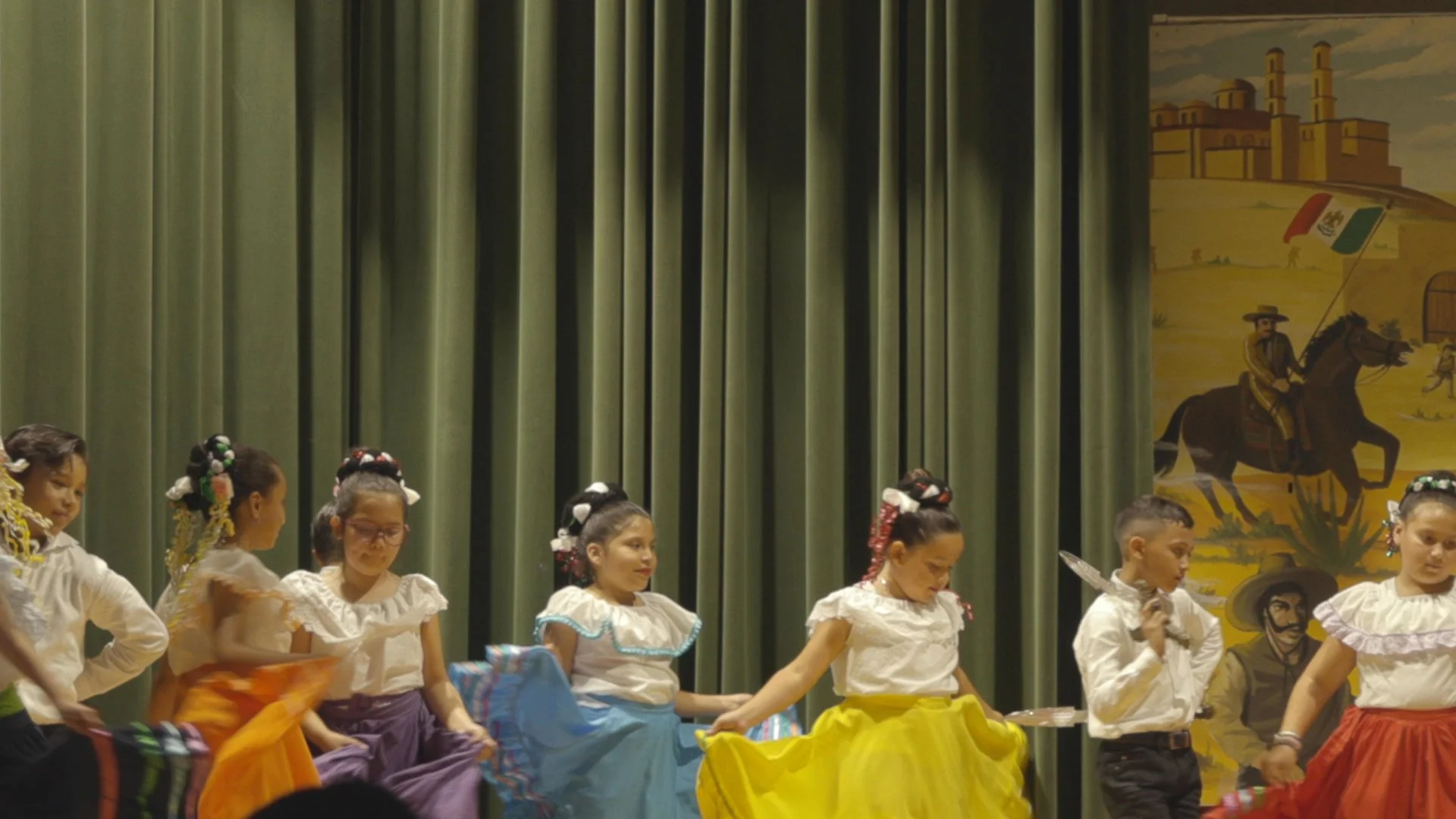 Students performing traditional Mexican folklórico dance on stage