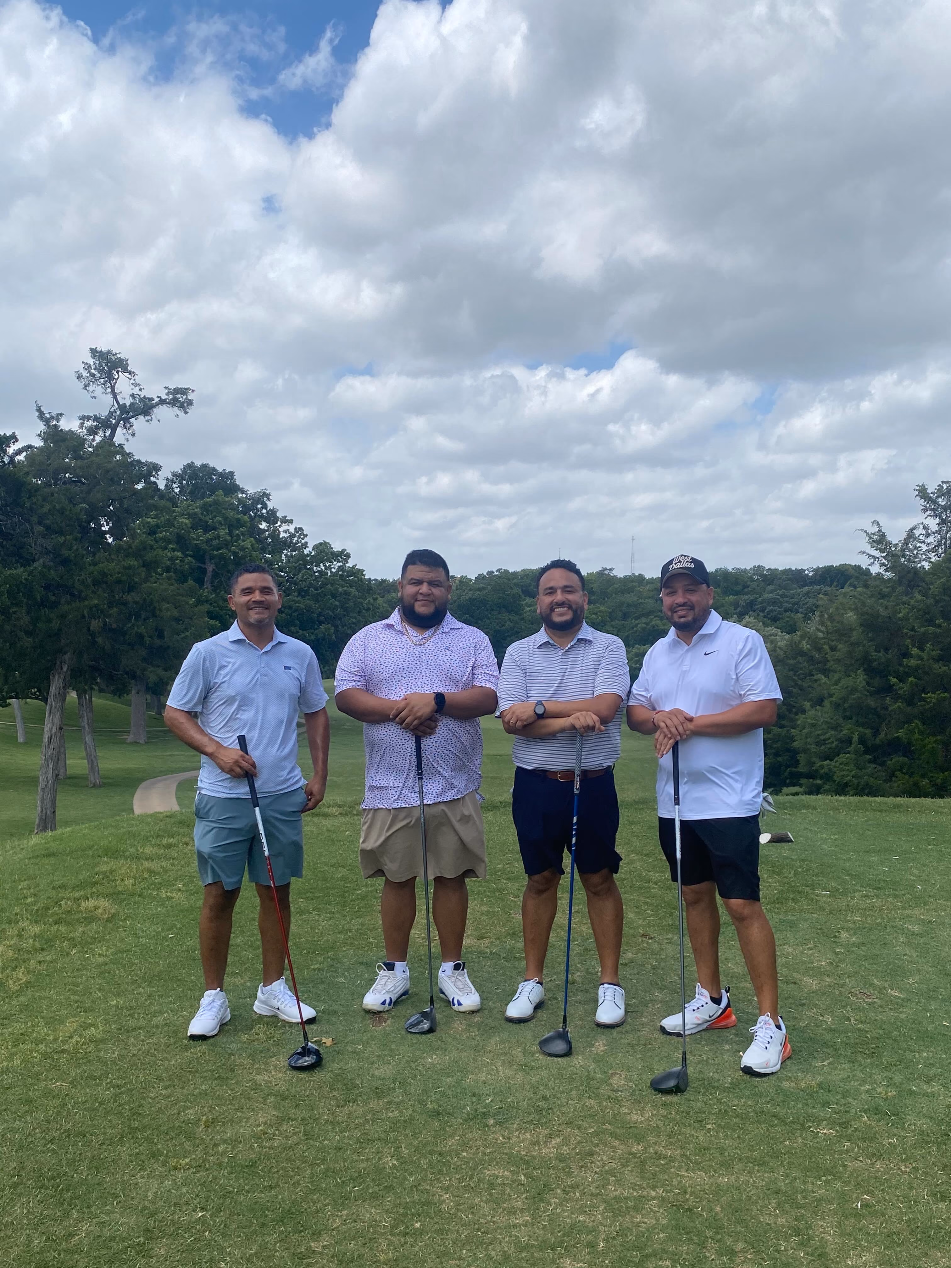 Four men posing with golf clubs on a golf course