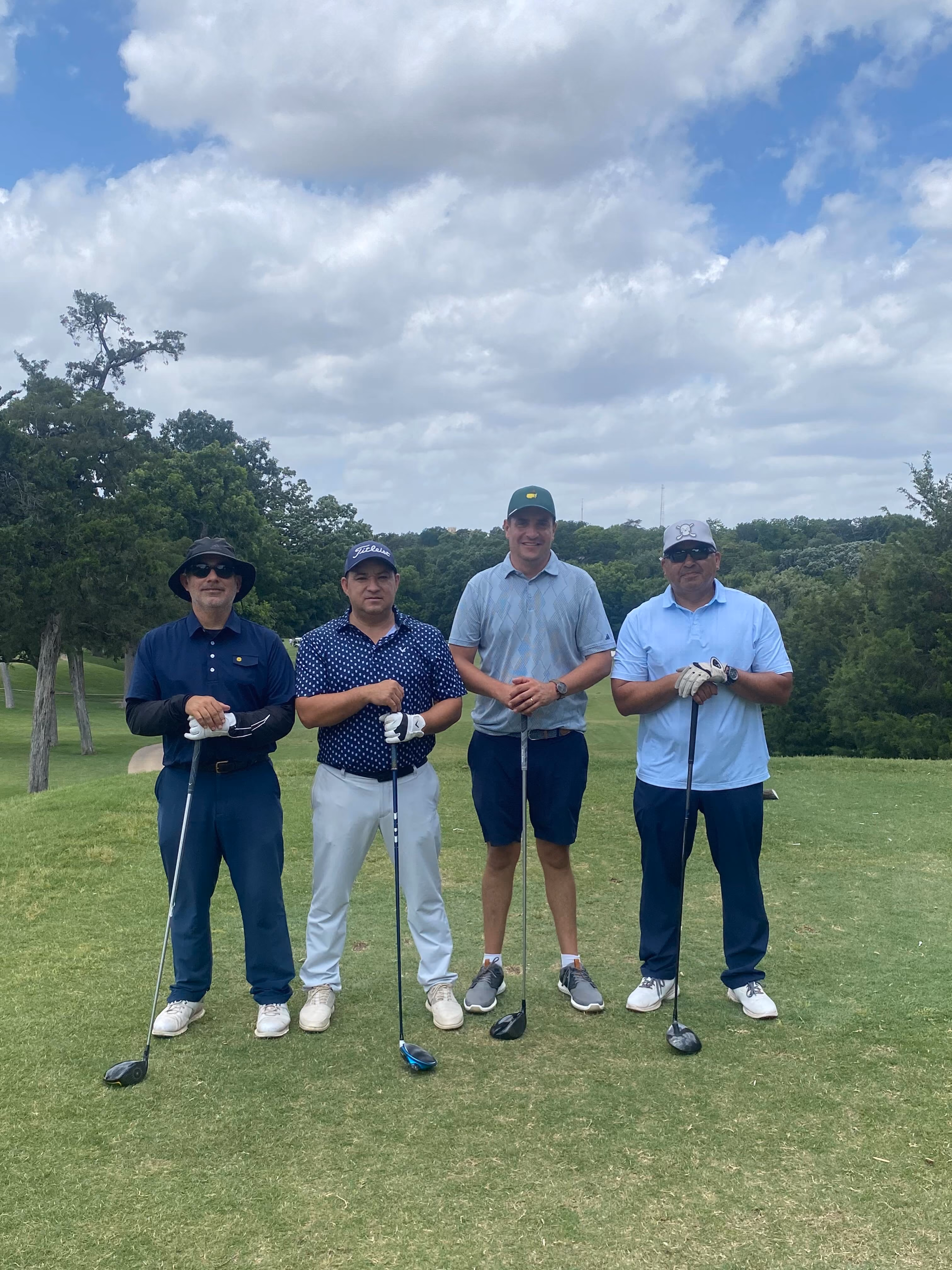 Four golfers posing together on a golf course with clubs