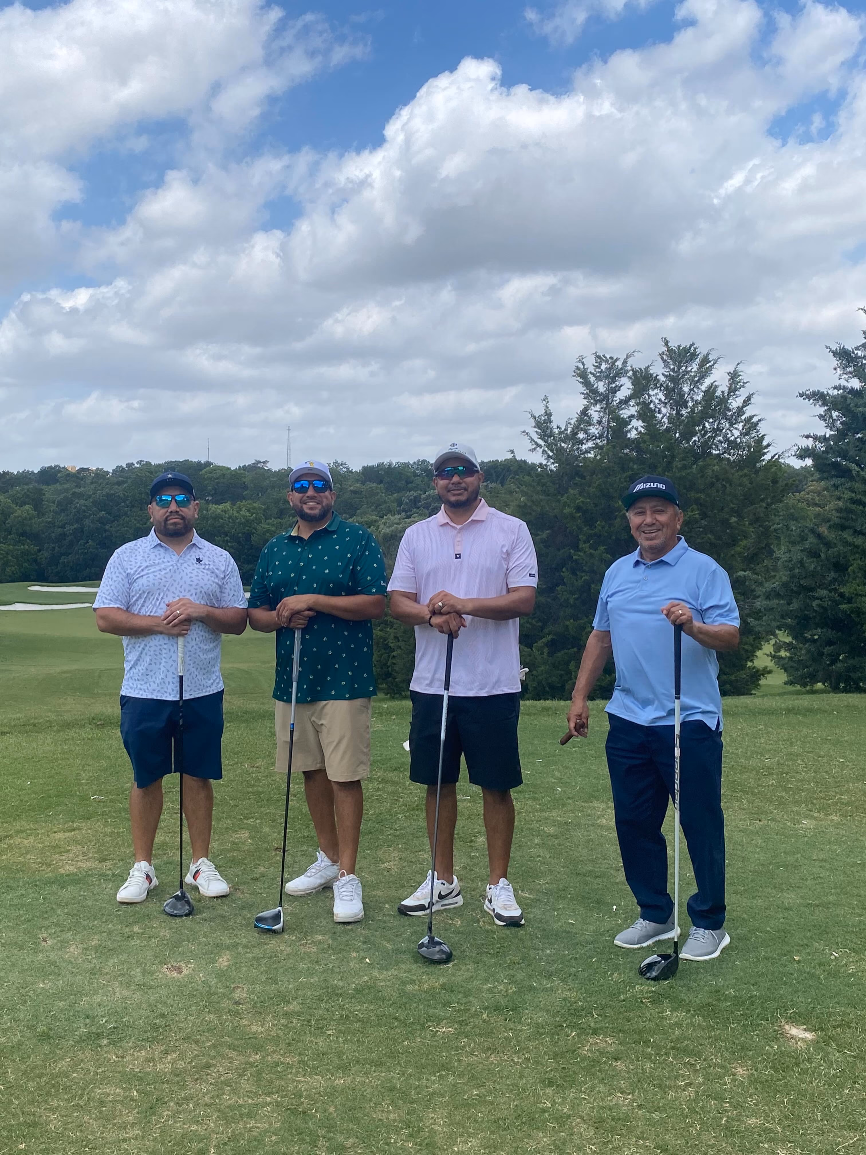 Four men posing with golf clubs on a golf course