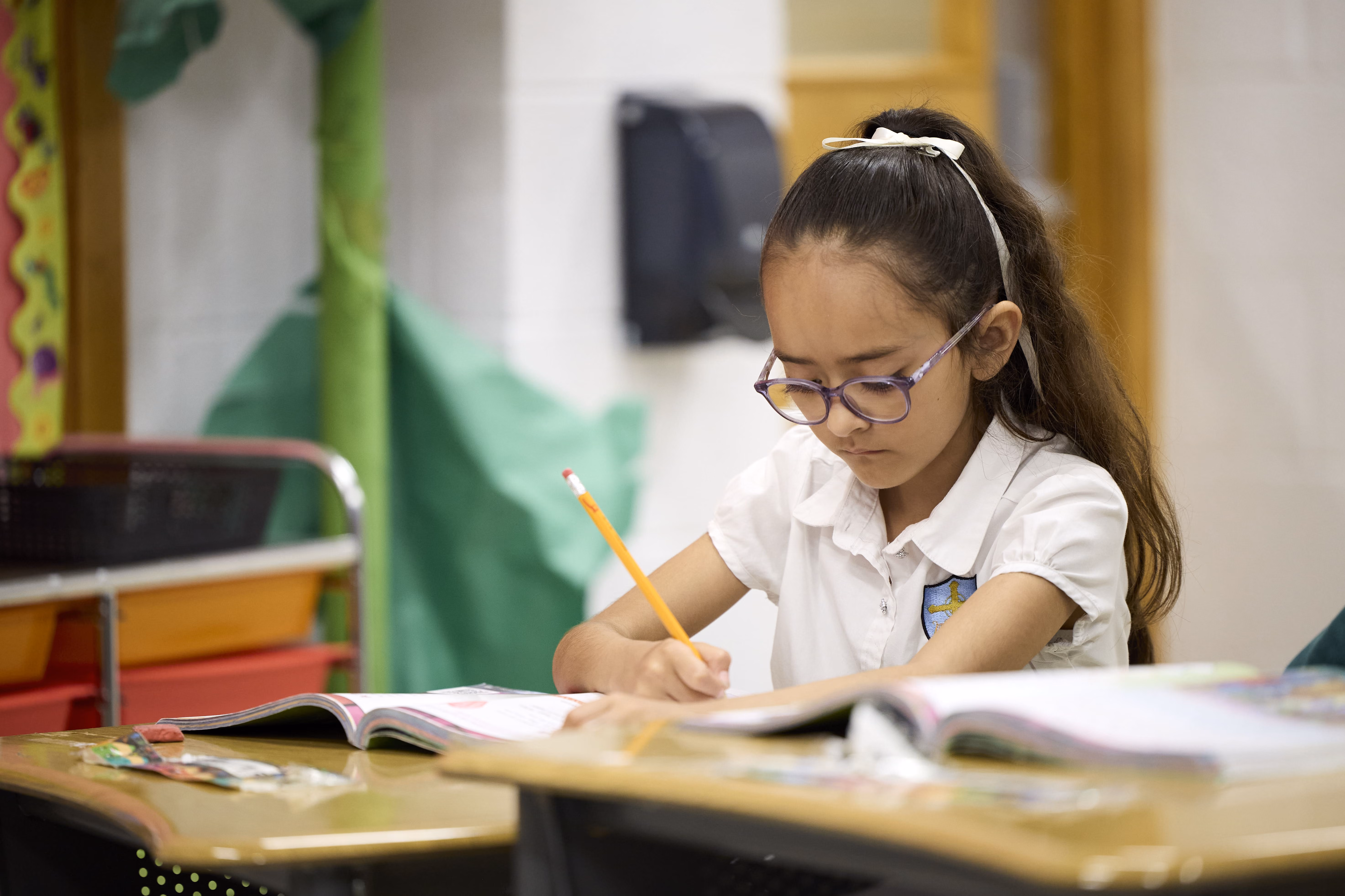 Student in uniform writing with pencil in open workbook at desk
