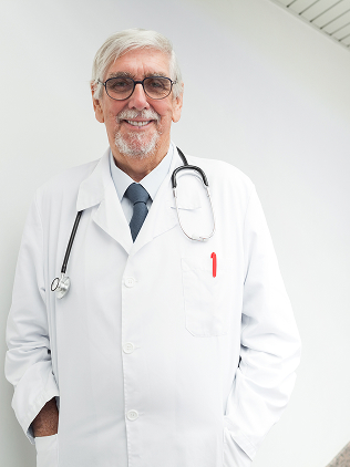 Smiling elderly male doctor with gray hair and glasses, wearing a white coat and stethoscope.