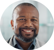 Smiling male doctor with a beard wearing a white coat in a clinical setting.