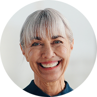 Smiling older woman with gray hair and bangs against a blurred background.