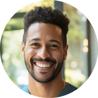 Smiling young man with curly hair and a beard in a bright indoor setting.