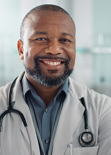 Smiling male doctor with a beard wearing a white coat and stethoscope.
