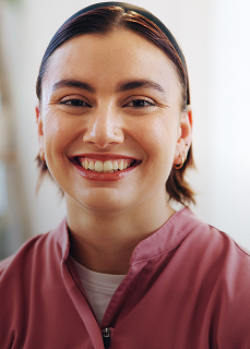 Smiling woman with short hair wearing a zip-up mauve jacket in a softly lit indoor setting.