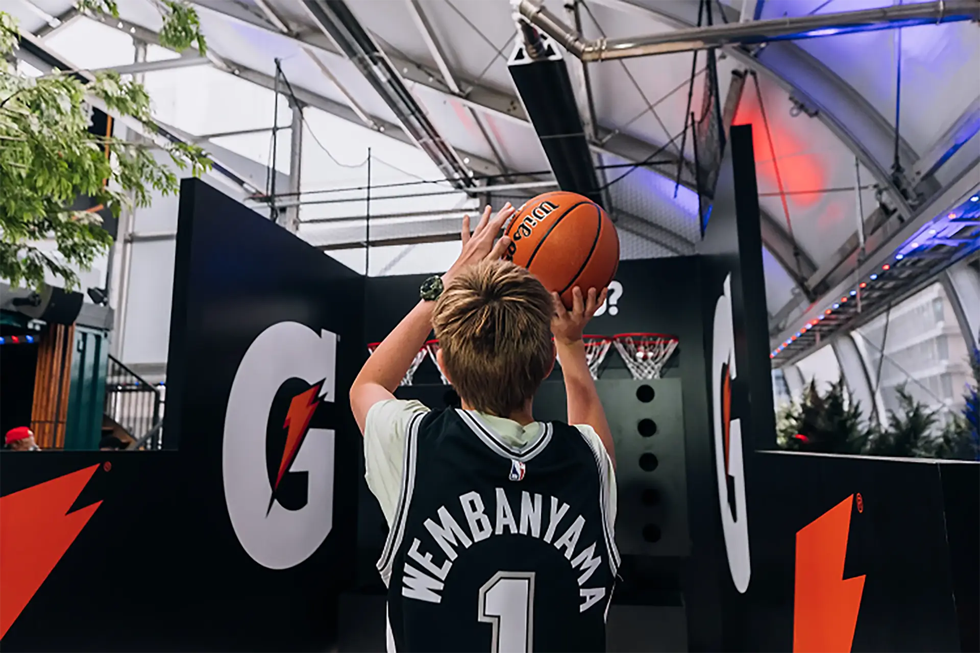 Indoor NBA-themed event space illuminated with purple lights, featuring hanging championship banners, lounge seating, and merchandise displays.
