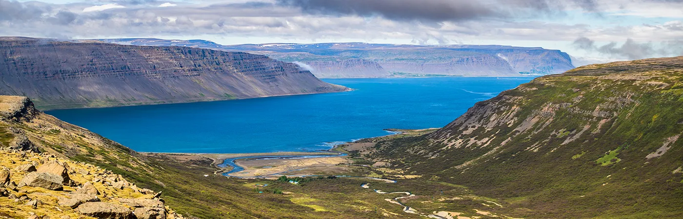 Panoramic Icelandic fjord with green hills and deep blue waters, highlighting nature tourism and fragile coastal ecosystems