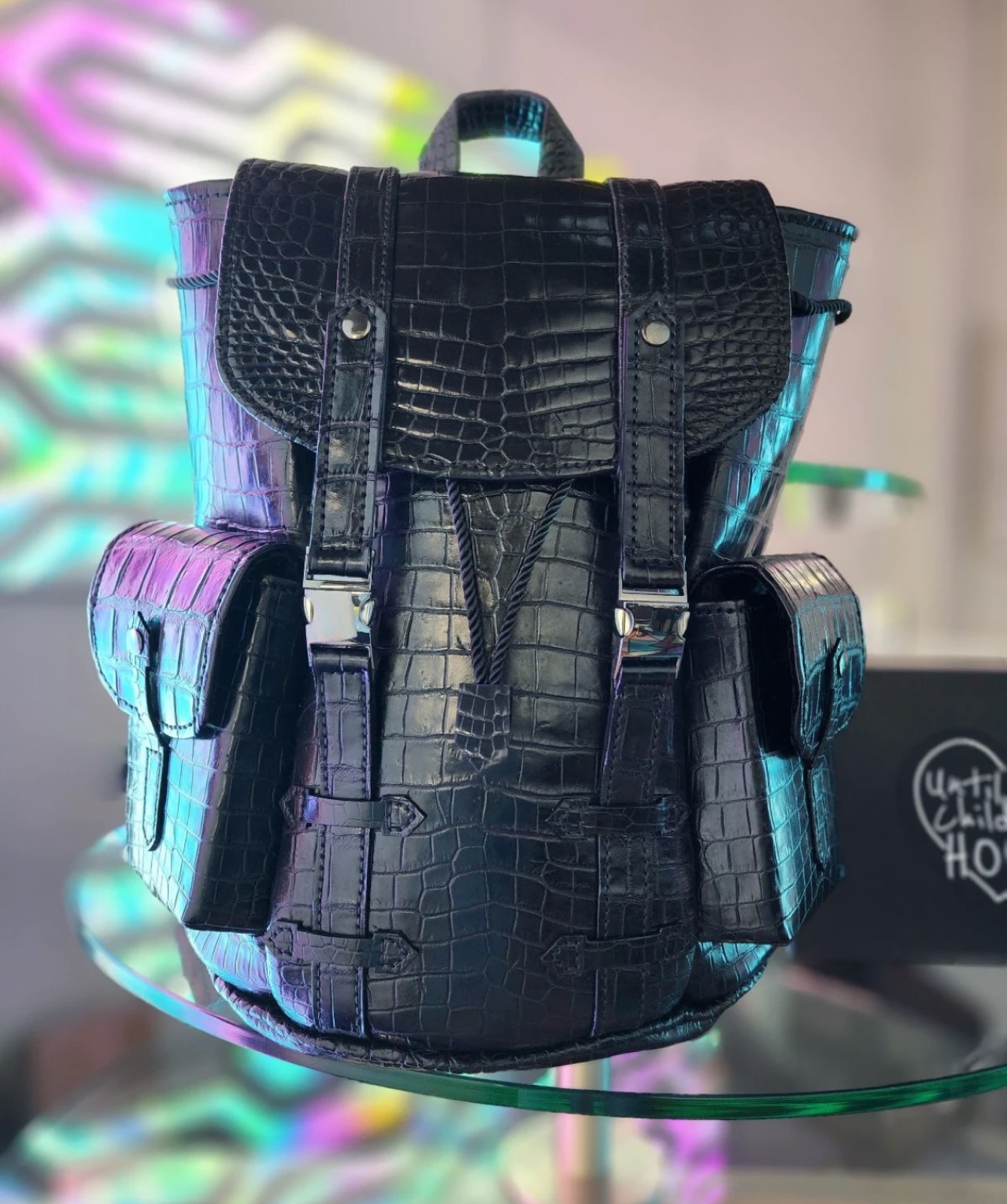 Frank Harkins alligator backpack in glazed jet black American alligator, with a scaled flap, twin buckled straps, drawstring closure and two side pockets.