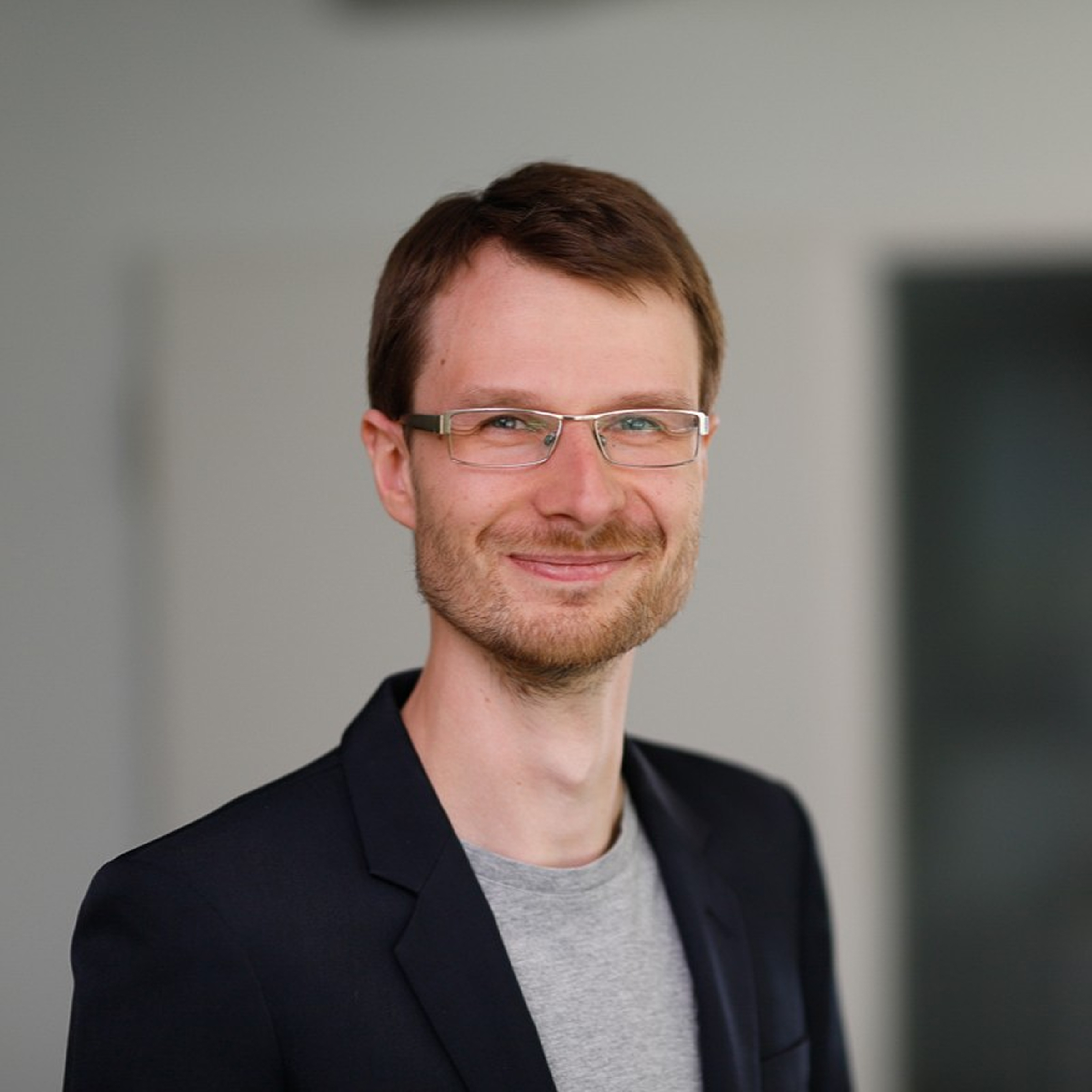 Thomas Ramson, Engineering Manager Lead at voize, wearing glasses and a blazer, smiling in the office.