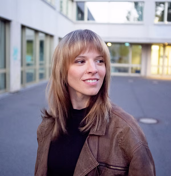 Luise Kreisel, Senior Product Manager Senior Care bei voize, lächelnd in brauner Lederjacke vor heller Gebäudefassade.