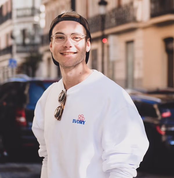 Marius Busen, Chief of Staff bei voize, lächelnd in weißem Sweatshirt mit Brille und Kappe auf der Straße.
