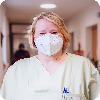 Pflegekraft der Kleeblatt Pflegen & Wohnen in heller Dienstkleidung trägt eine FFP2-Maske im Pflegeheim.
