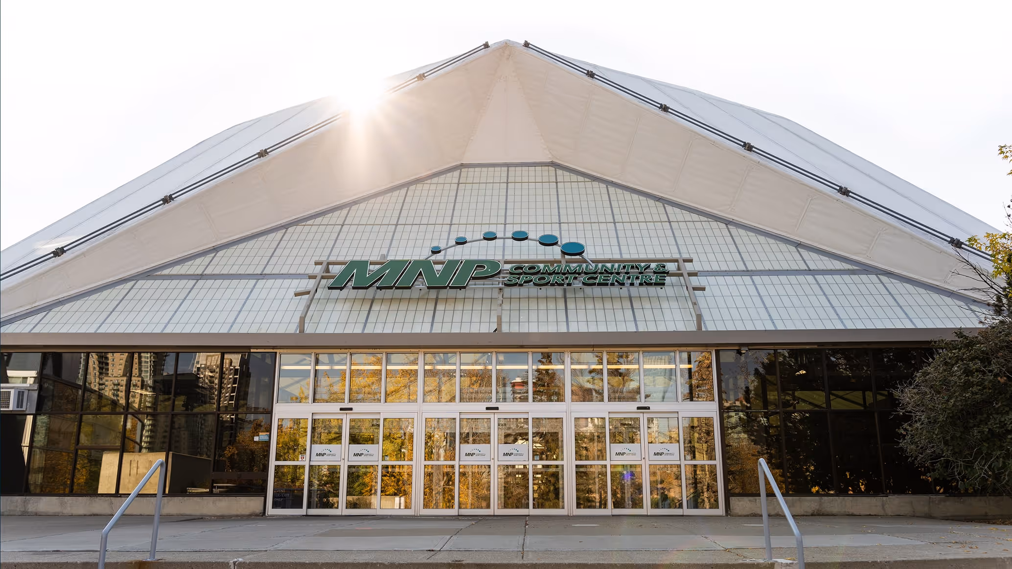 Front entrance of the MNP Community & Sport Centre with a large glass façade and sunlight above the roof peak.