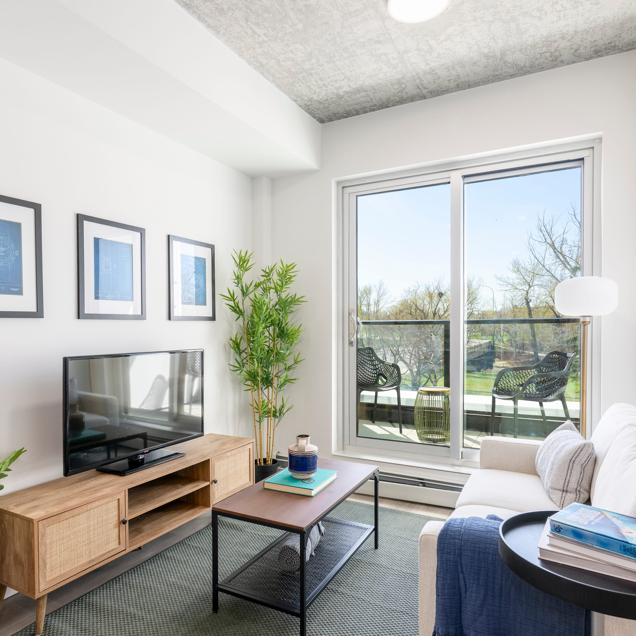 Modern living room with sofa, TV on wooden stand, coffee table, and balcony with chairs outside.