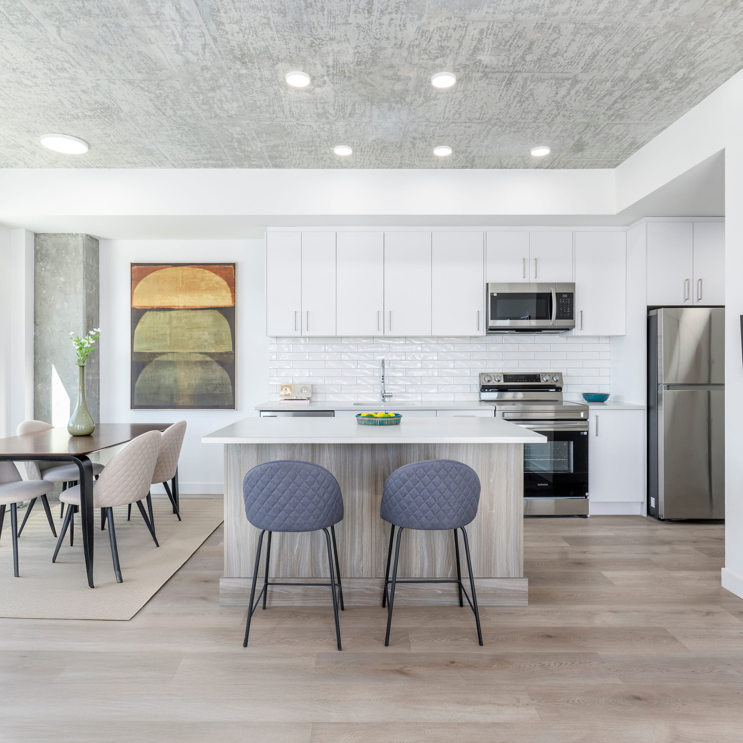 Modern kitchen with white cabinets, stainless steel appliances, island with two gray stools, and dining table.