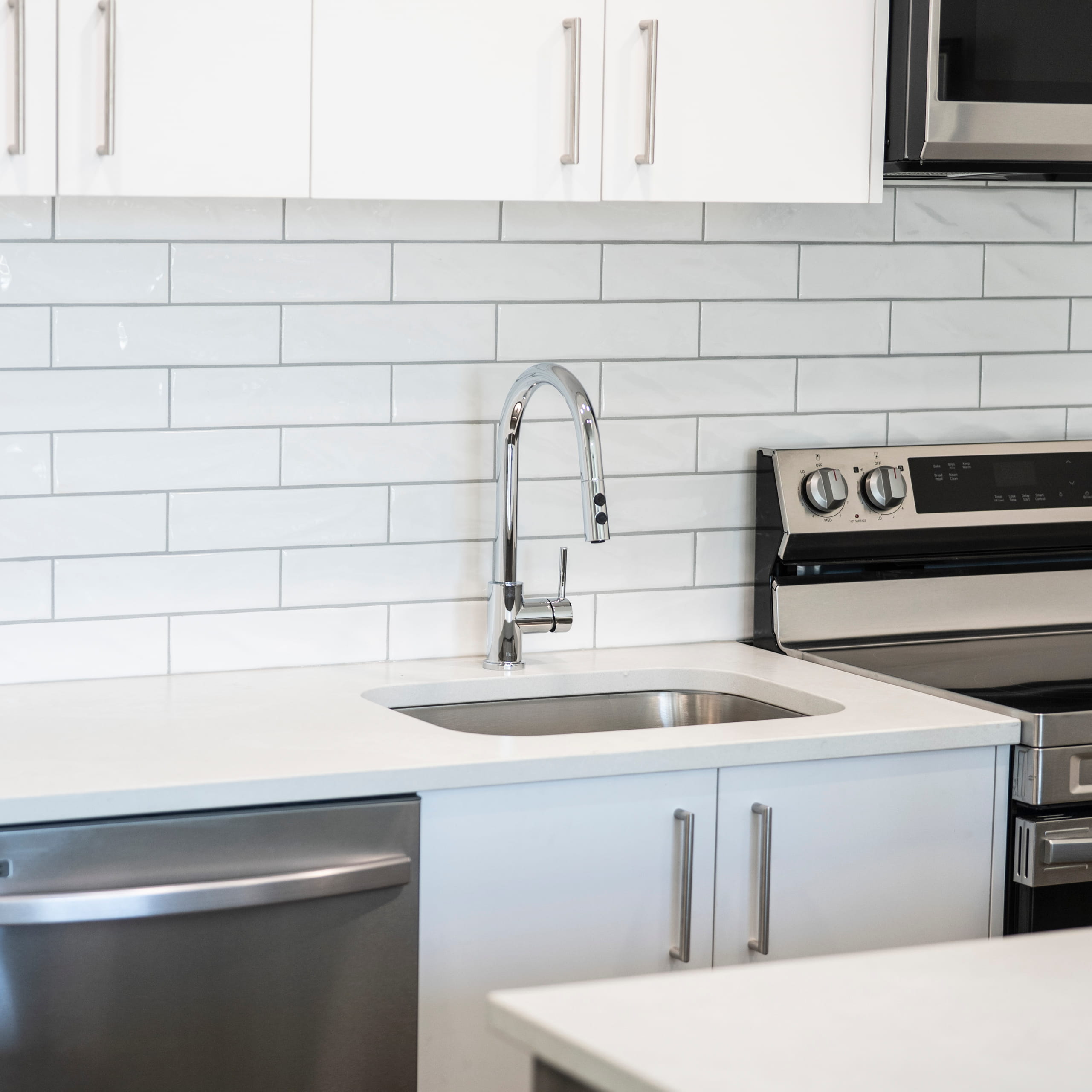 Modern kitchen sink with chrome faucet, white cabinets, subway tile backsplash, stainless steel stove and dishwasher