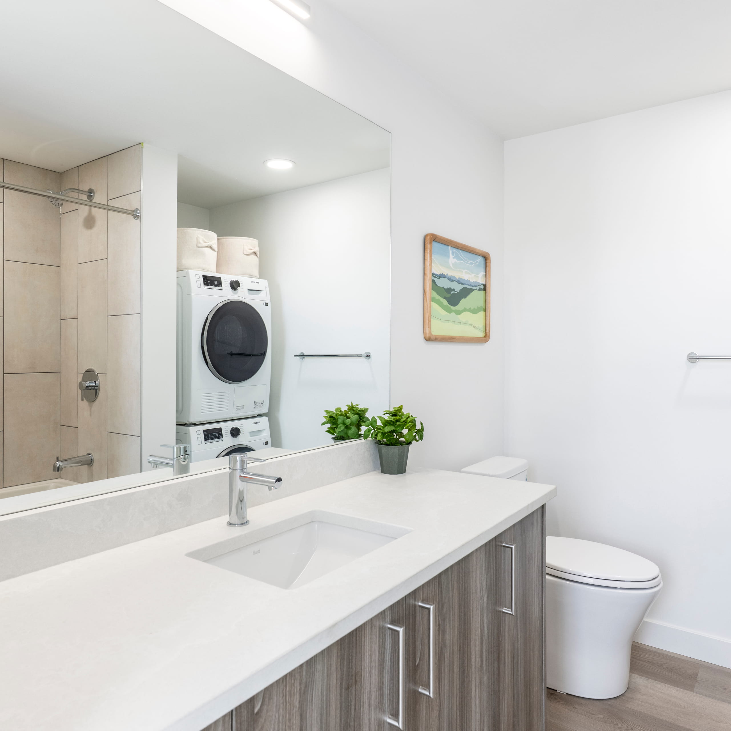 Modern bathroom with wood vanity, white countertop, sink, toilet, and stacked washer and dryer.