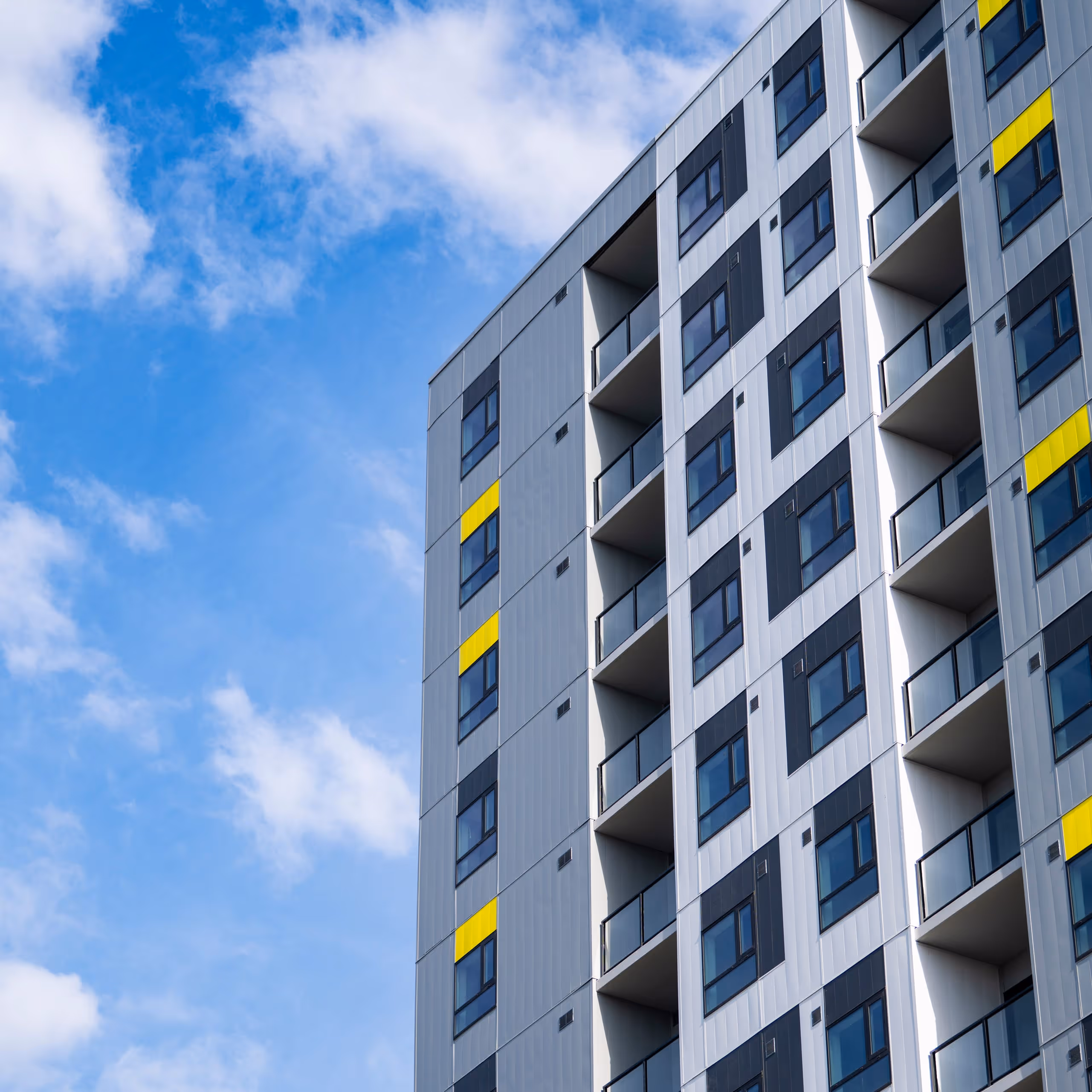 High-rise building facade with balconies, black and white panels, and yellow window accents under blue sky.