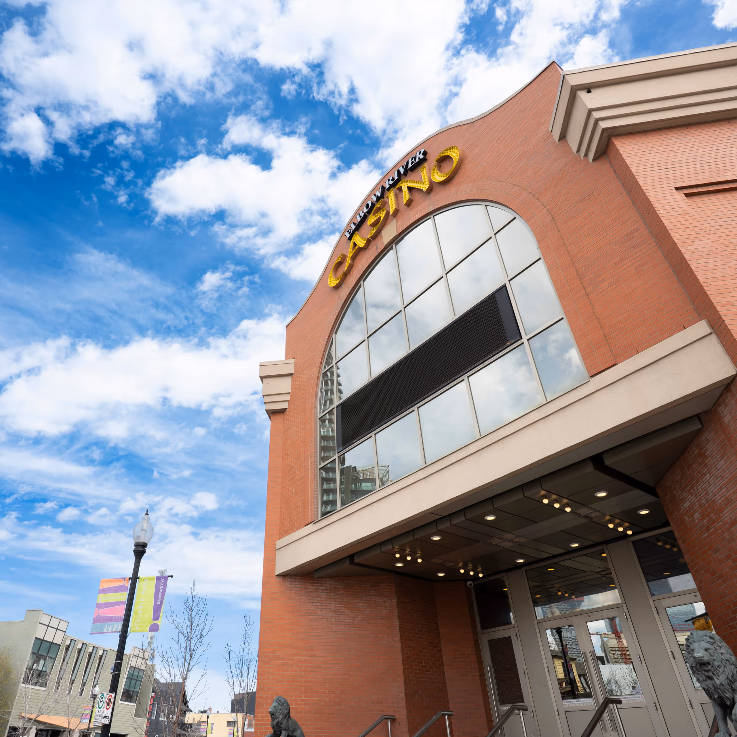 Entrance of Elbow River Casino with large windows and two lion statues under a blue sky.