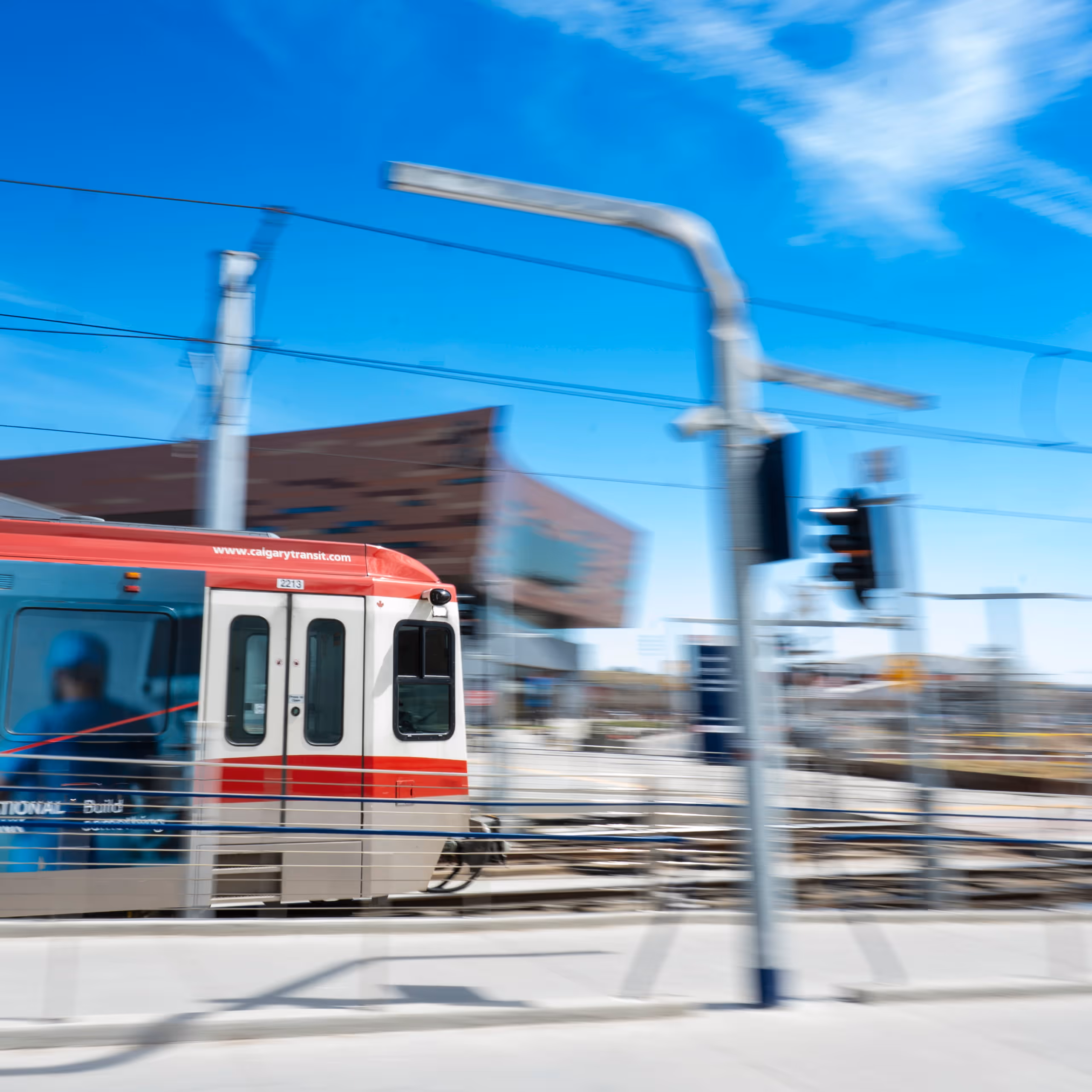 Calgary Transit light rail train moving past tracks under a blue sky with blurred background.