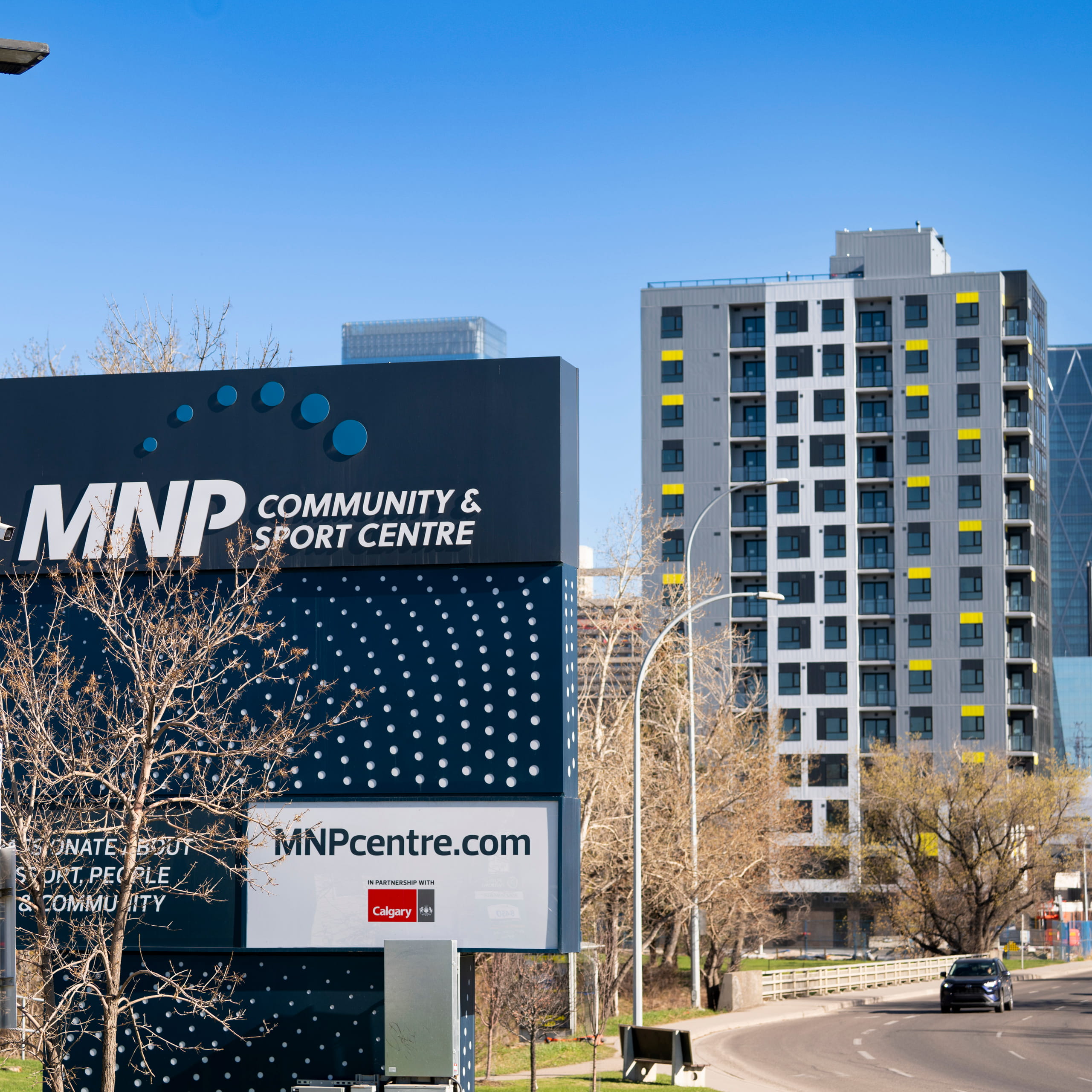MNP Community & Sport Centre sign beside a road with trees and a modern building in the background.