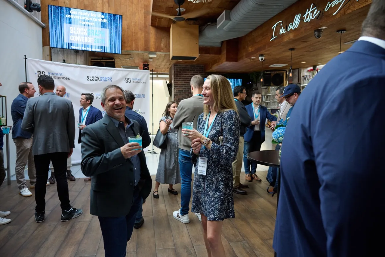 People socializing and holding drinks at a Blockgraph Converge 2023 networking event in a modern indoor venue.