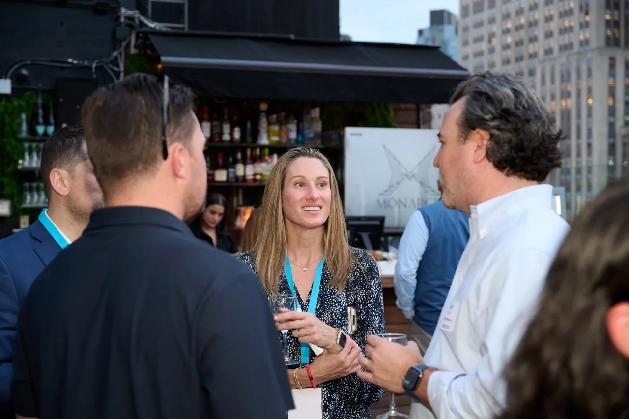 Group of people engaged in conversation at an outdoor social event with city buildings in the background.