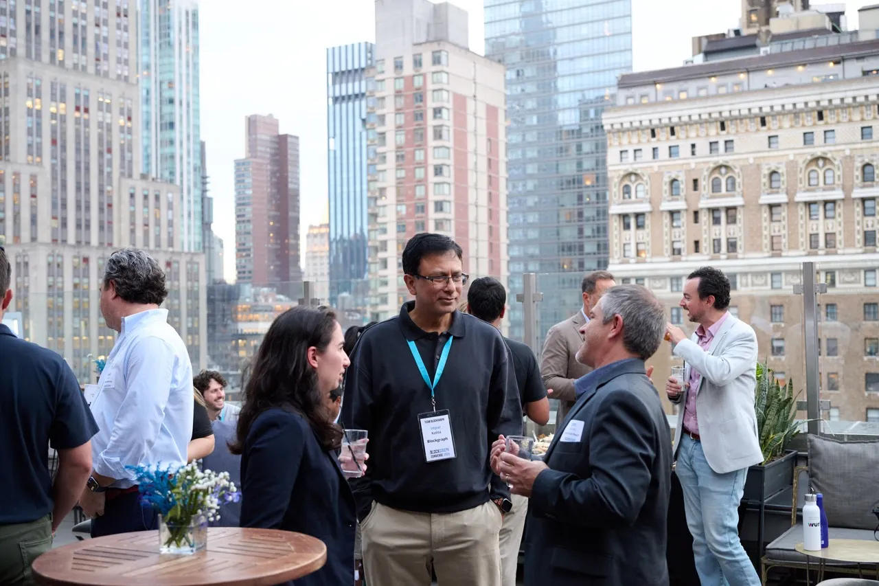 People socializing at an outdoor rooftop event in a city with tall buildings in the background.