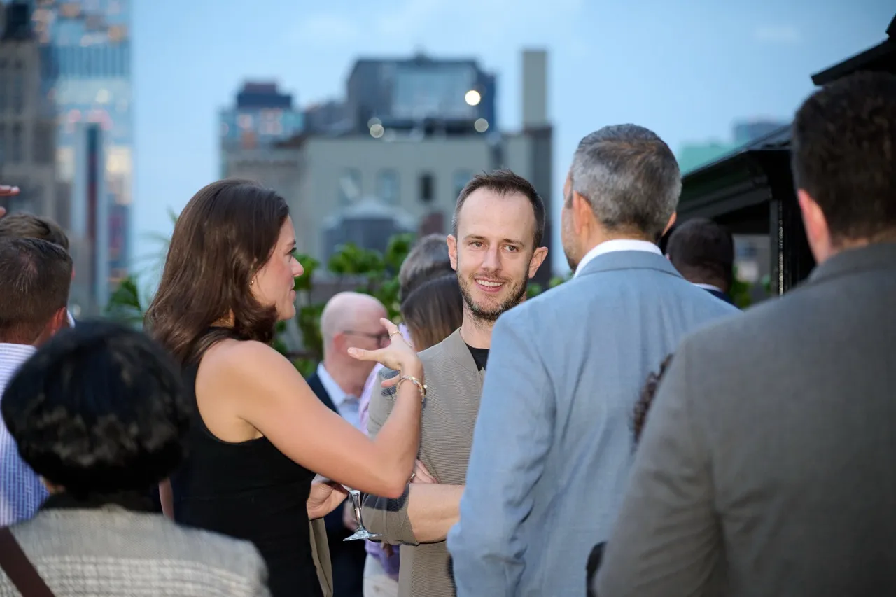 Group of people engaged in conversation at an outdoor event with city buildings in the background.