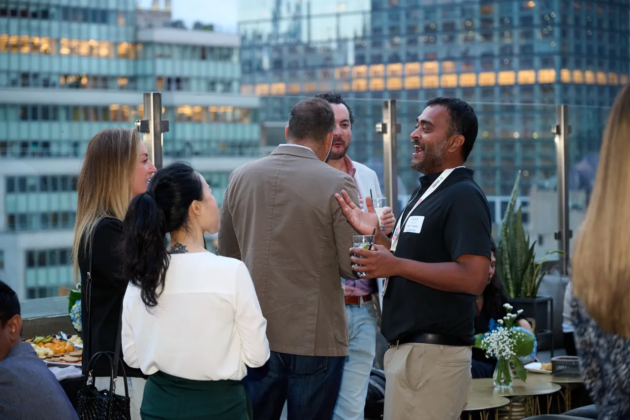 A group of five people socializing on a rooftop with city buildings in the background during evening.