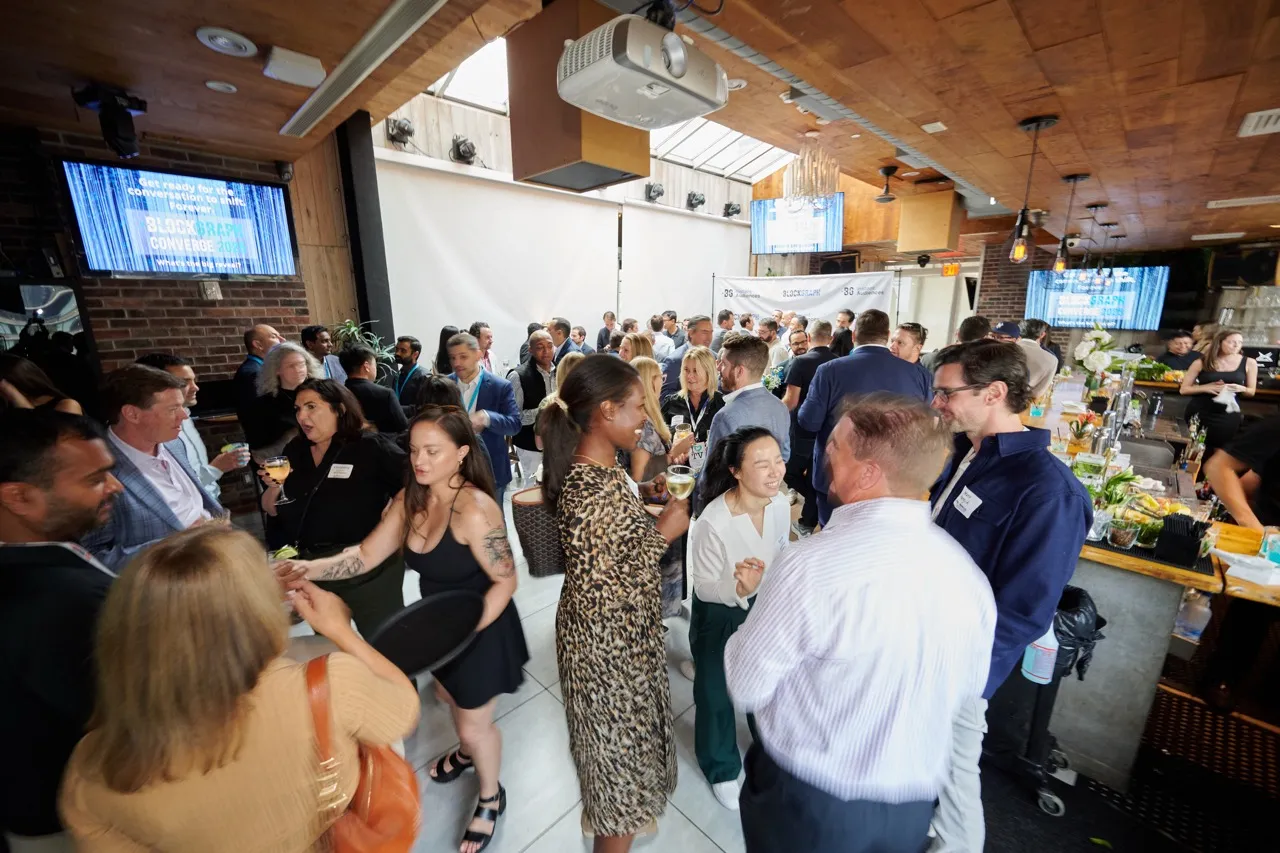 Crowd of diverse people socializing and networking in an indoor event space with drinks, screens, and a bar area.
