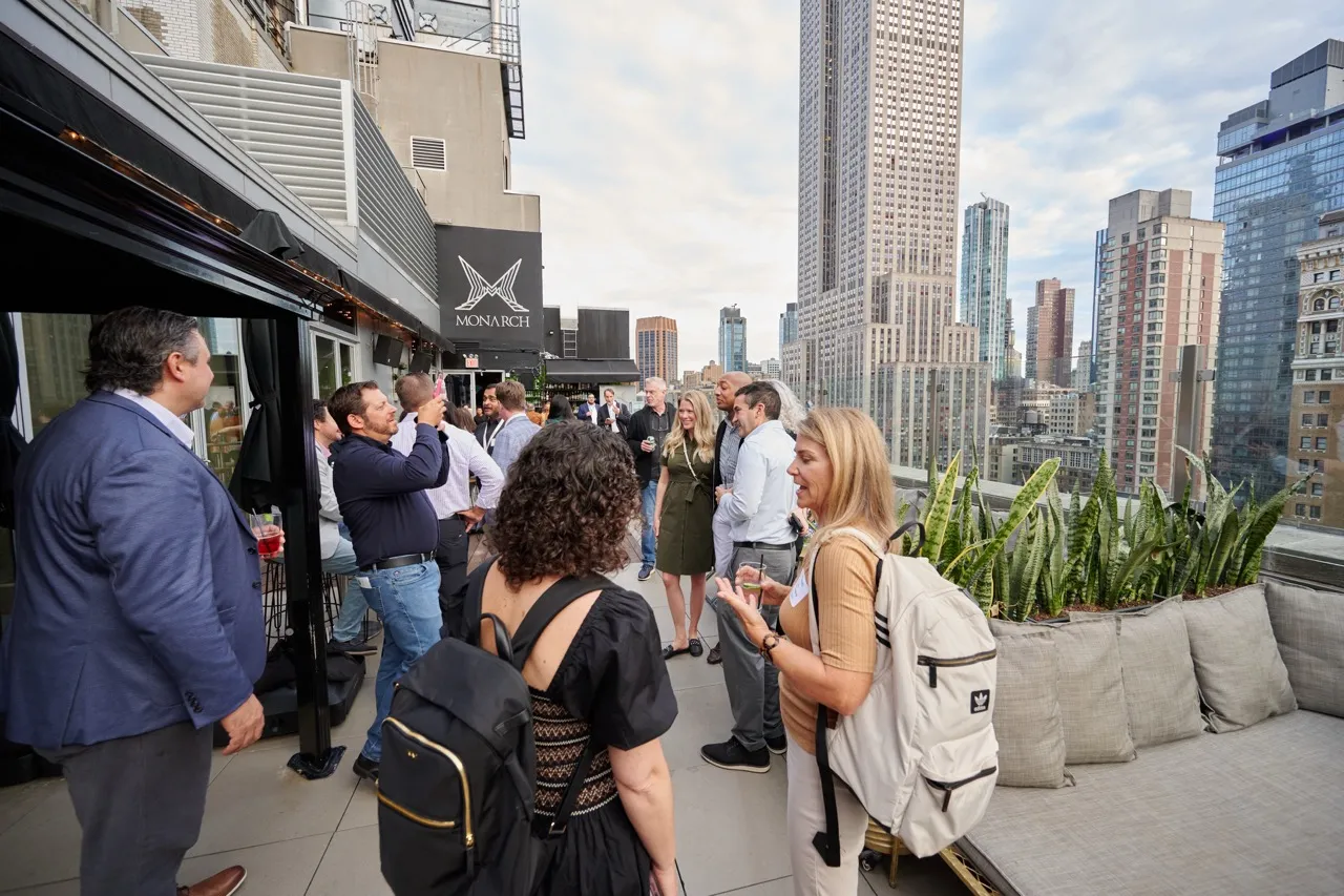 Group of people socializing on a rooftop terrace with city skyscrapers in the background.