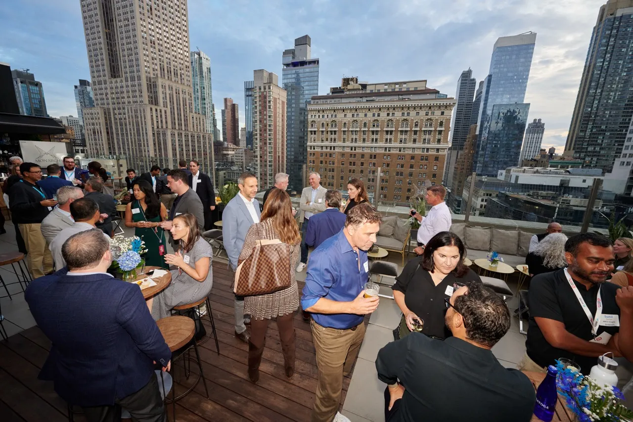 People socializing on a rooftop terrace with city skyscrapers in the background during a daytime event.