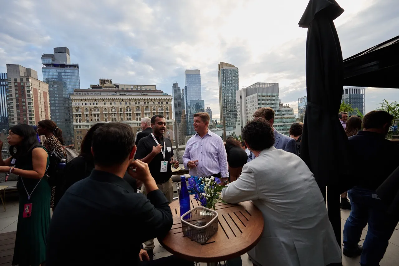People socializing on a rooftop patio with a city skyline in the background during cloudy weather.