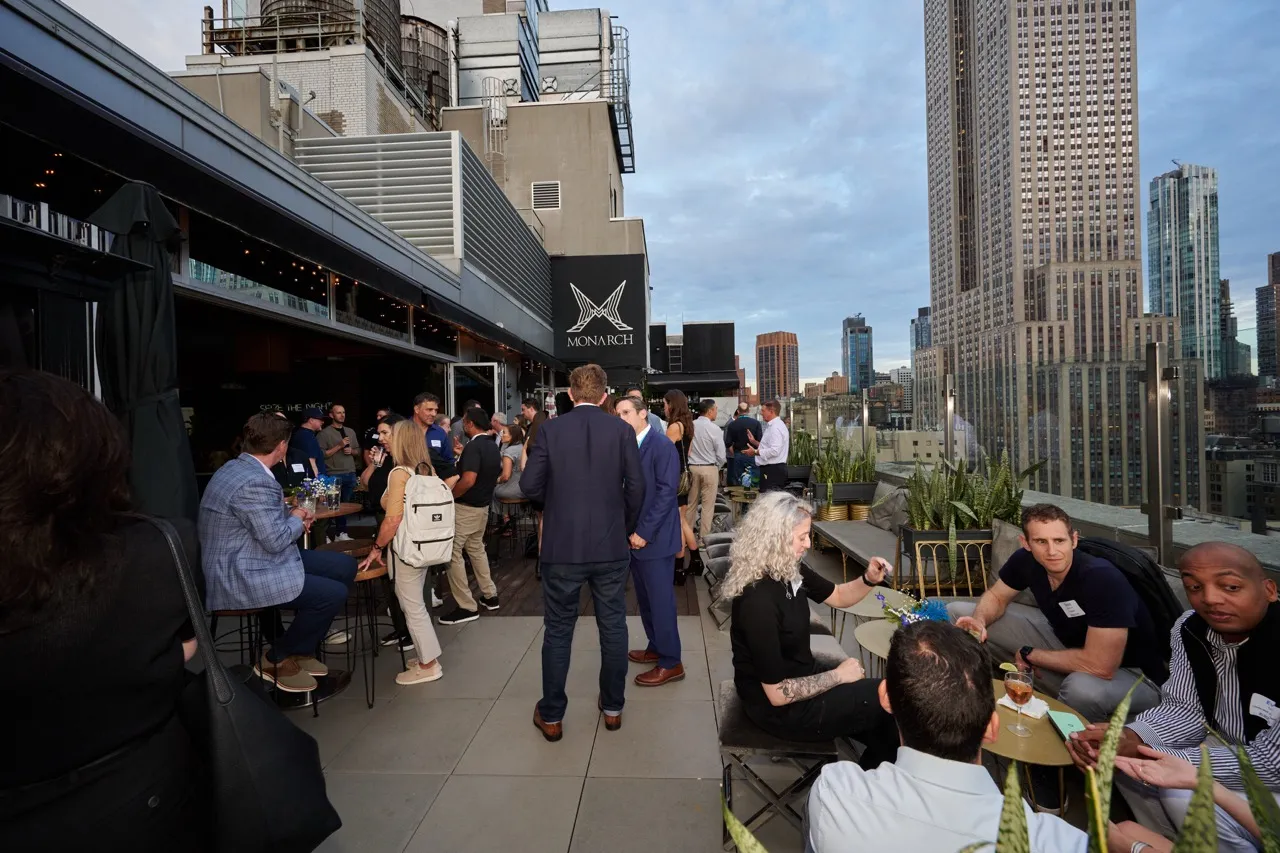 Outdoor rooftop networking event at Monarch with people socializing and city skyscrapers in the background.