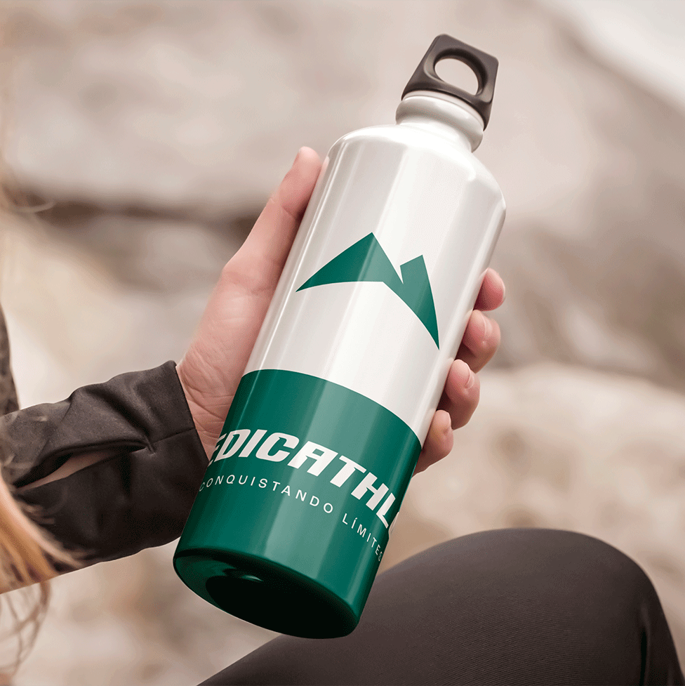 Mano sosteniendo botella de agua deportiva blanca y verde con logotipo de Medicathlon y tagline "Conquistando límites" sobre fondo de roca diseño de merchandise y activación de marca para empresa colombiana de deporte y salud por Intacto Studio estudio de branding en Medellín y Bogotá Colombia.