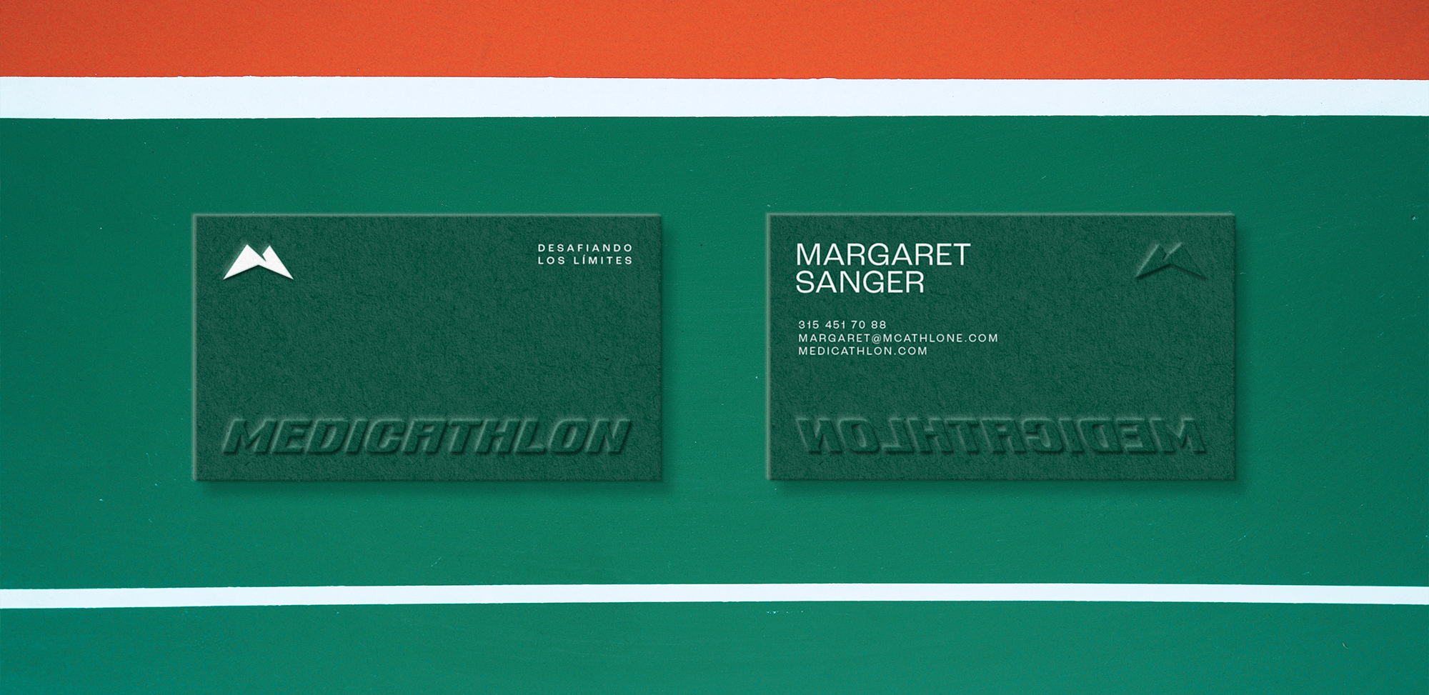 Tarjetas de presentación de Medicathlon en verde oscuro con logotipo de montaña y texto en relieve con tagline "Desafiando los límites" en el anverso y datos de contacto en el reverso sobre fondo con franjas verde naranja y blanco diseño de papelería corporativa y sistema de identidad visual para marca colombiana de deporte y salud por Intacto Studio estudio de branding en Medellín y Bogotá Colombia.