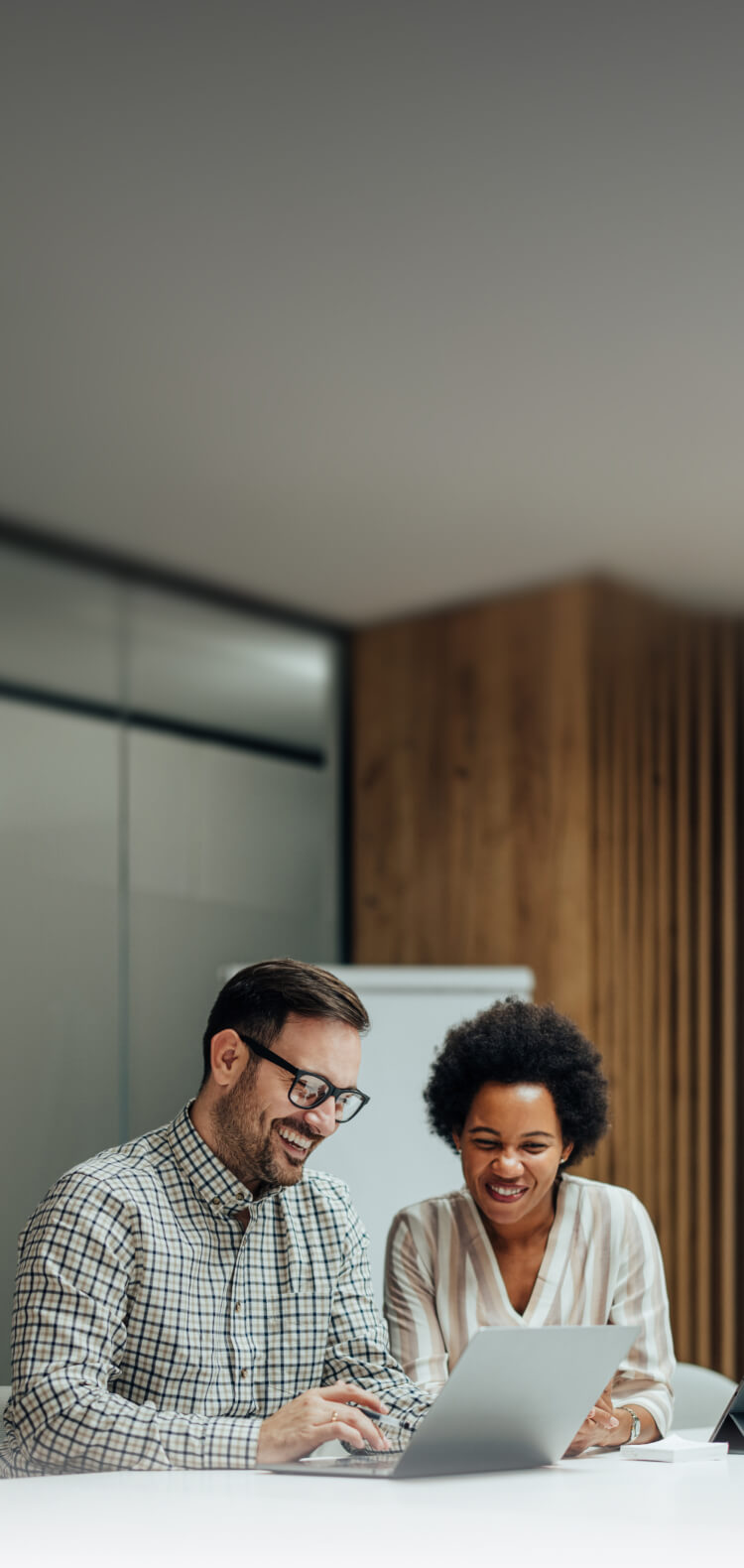 Smiling man and woman sitting at a white table working together on a laptop in a modern office.