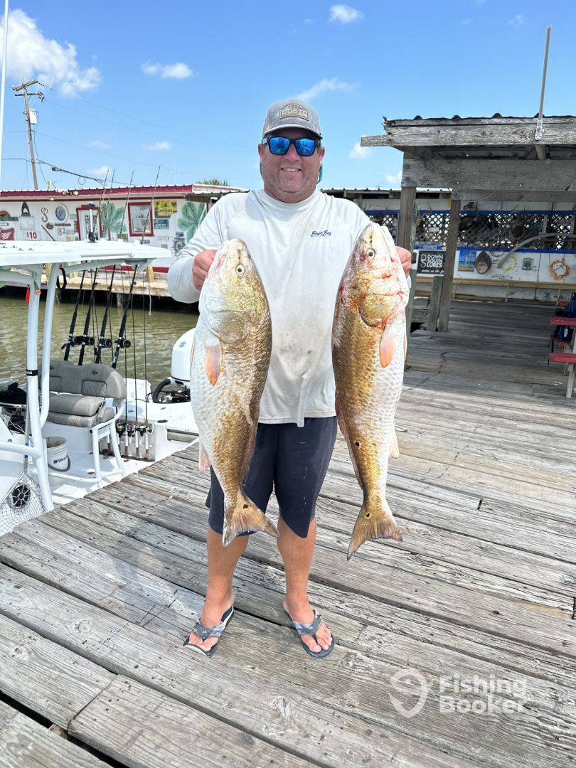 captain corey bickforrd holding out two massive red fish while fishing with reel adventures