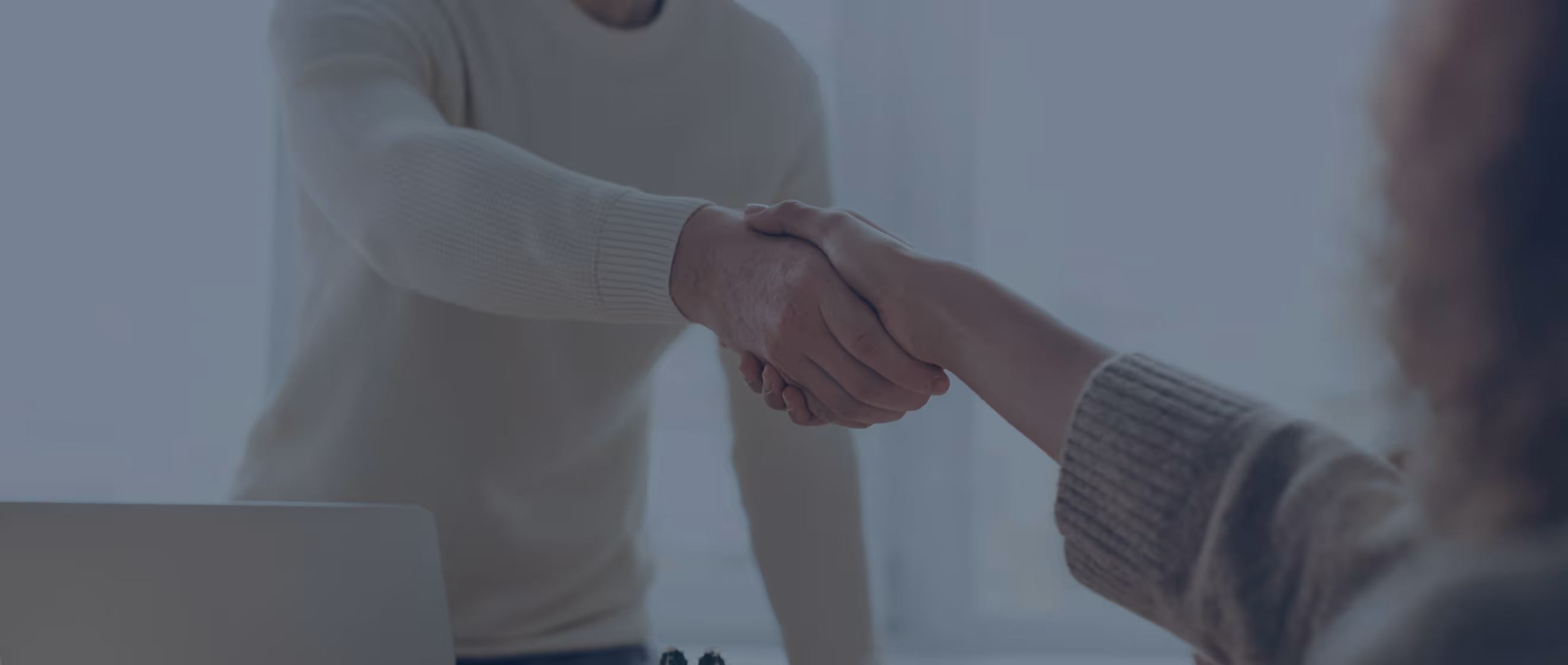 Two people shaking hands across a desk in a professional setting.