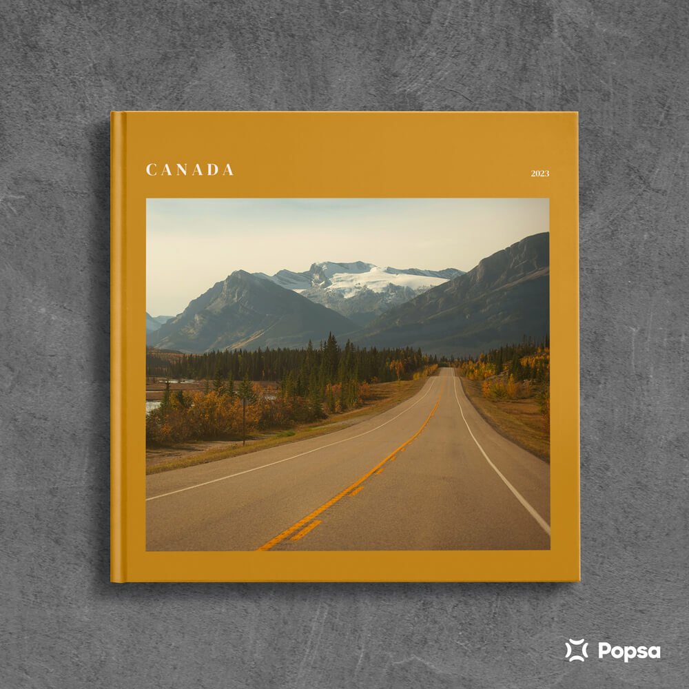 Popsa photobook with a mustard-yellow cover featuring a photograph of a road leading towards the Canadian Rocky Mountains.