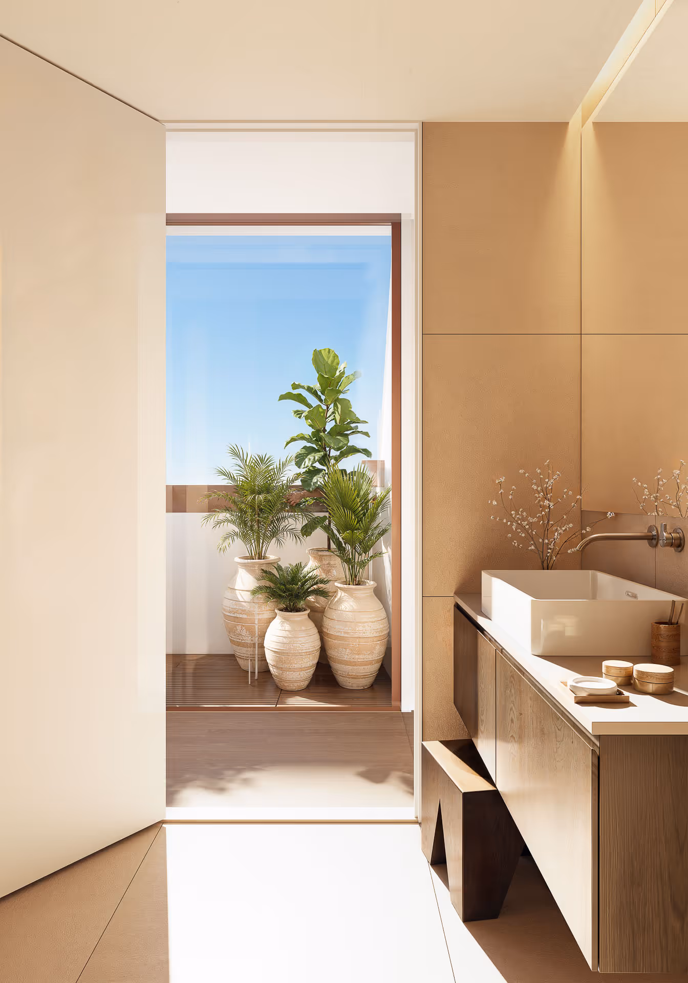 Casa de banho moderna com lavatório quadrado, decoração em tons neutros e vasos com plantas verdes na varanda ao fundo.